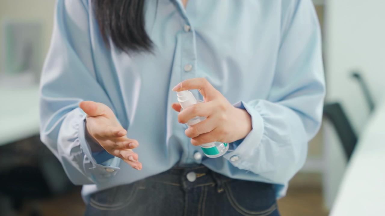 職場で消毒スプレーで手を消毒している、顔が特定できない女性ビジネスパーソン。疫病やパンデミック対策として、女性が手のひらにアルコール抗菌スプレーを噴霧し、細菌や微生物を除去している様子。