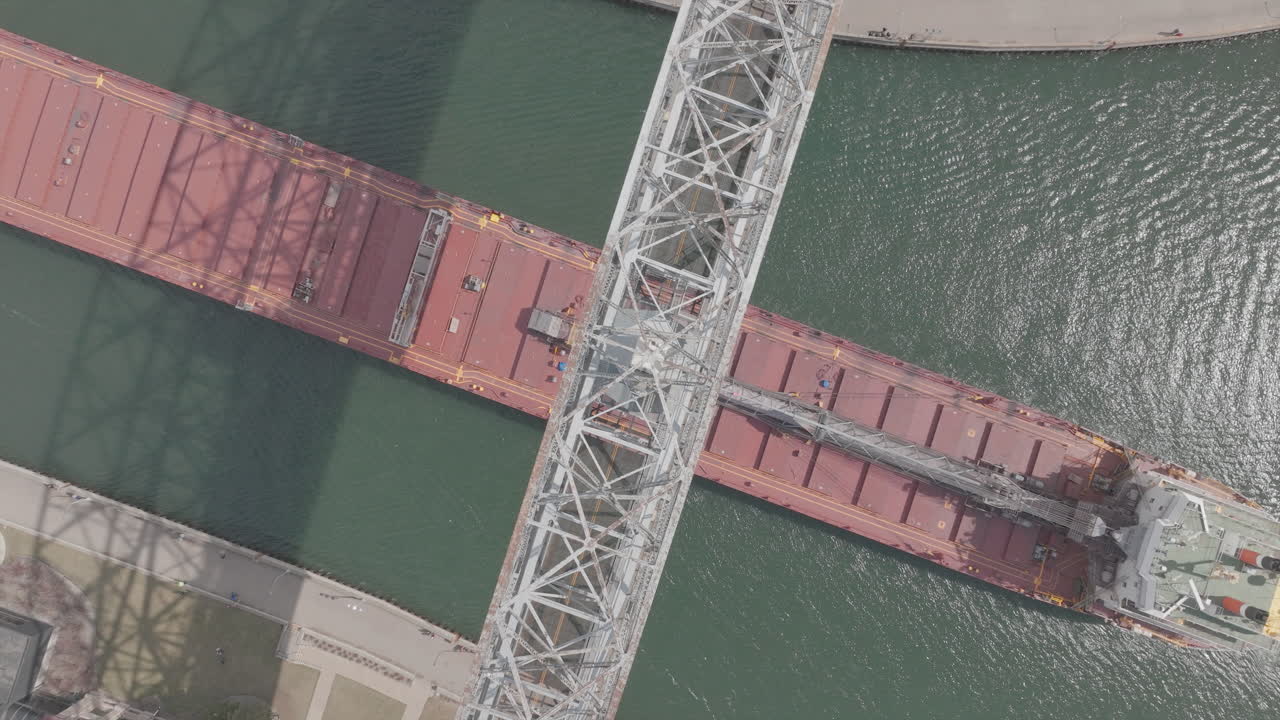 una imagen aérea de arriba hacia abajo de un buque de carga que pasa por debajo del puente de elevación aérea en duluth, minnesota