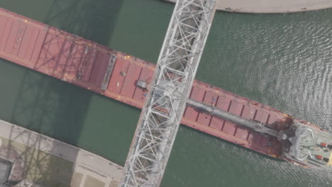 Antena-De-Arriba-Hacia-Abajo-Del-Buque-De-Carga-Que-Pasa-Bajo-El-Puente-Elevador-Aéreo-En-Duluth,-Minnesota