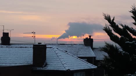 Schornstein-Der-Rauchindustrie-über-Gefrorenen-Dächern-Von-Winterhäusern,-Die-Den-Orangefarbenen-Himmel-Des-Sonnenaufgangs-Leuchten