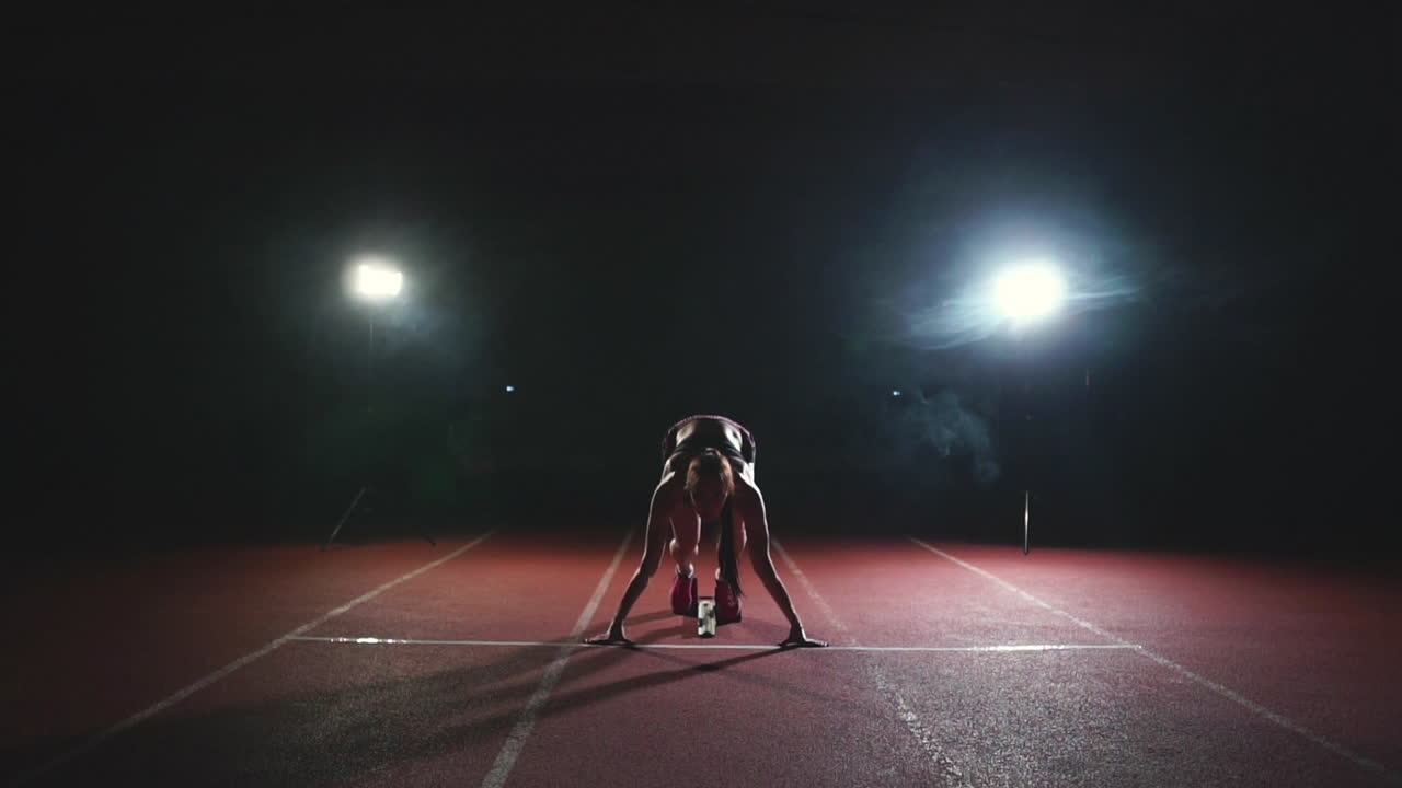 atleta femenina en un fondo oscuro se está preparando para correr el sprint de cross-country desde las almohadillas en la cinta de correr en un fondo oscuro