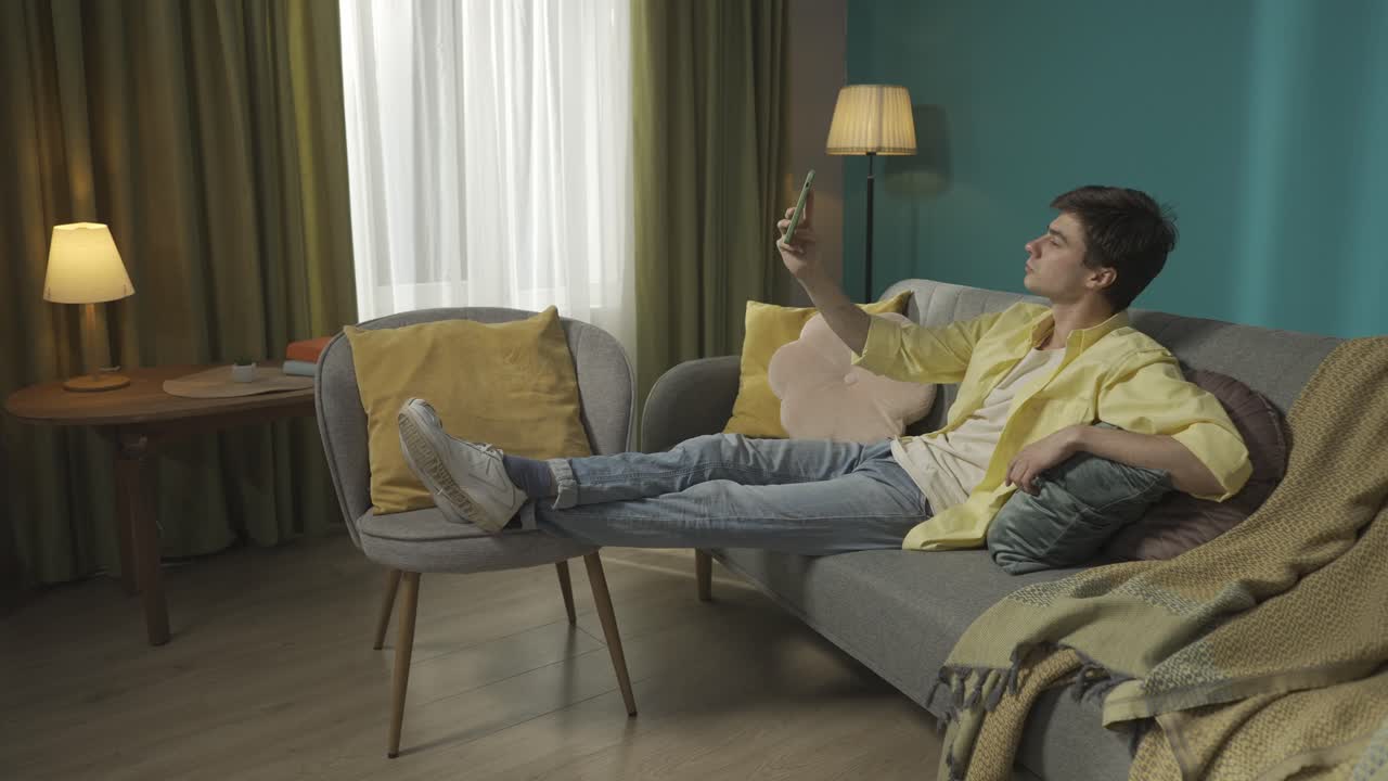 Young Man Relaxing on Sofa Using Smartphone