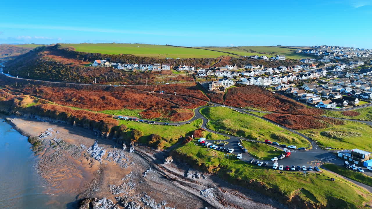 Vista aérea de casas de vila costeira e estacionamento de praia. Vista elevada de edifícios residenciais, um parque de estacionamento e colinas relvadas perto do mar na costa de Southerndown.