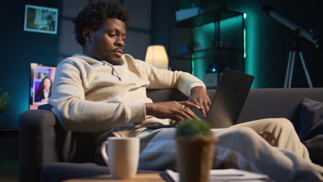 freelancer at home focused on online research and surfing the internet, utilizing a laptop for telework and staying connected in a digital world. browsing the social media on his couch. camera b.