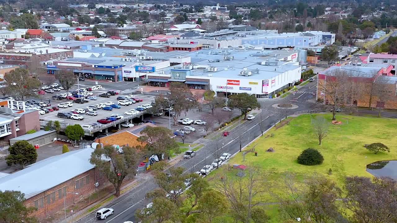 Un dron sobrevuela un centro urbano regional con complejos comerciales, aparcamientos y zonas verdes.