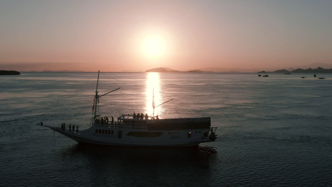 A right to left pan drone shot of a boat in the sea during the sunset with beautiful sun reflection.