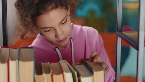 preteen school girl selecting relaxing interesting book to read from bookshelf taking a rest on sofa