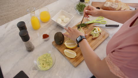 adding herbs to healthy avocado toast, woman in kitchen with fresh ingredients