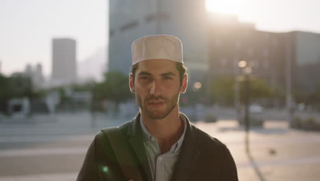 close up portrait of attractive confident middle eastern man looking serious at camera pensive in urban city background wearing kufi hat sunset