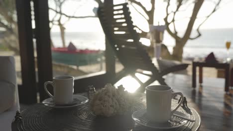 static shot 2 white steaming mugs on a small table in a tropical luxury villa with the sunny ocean in the distant background