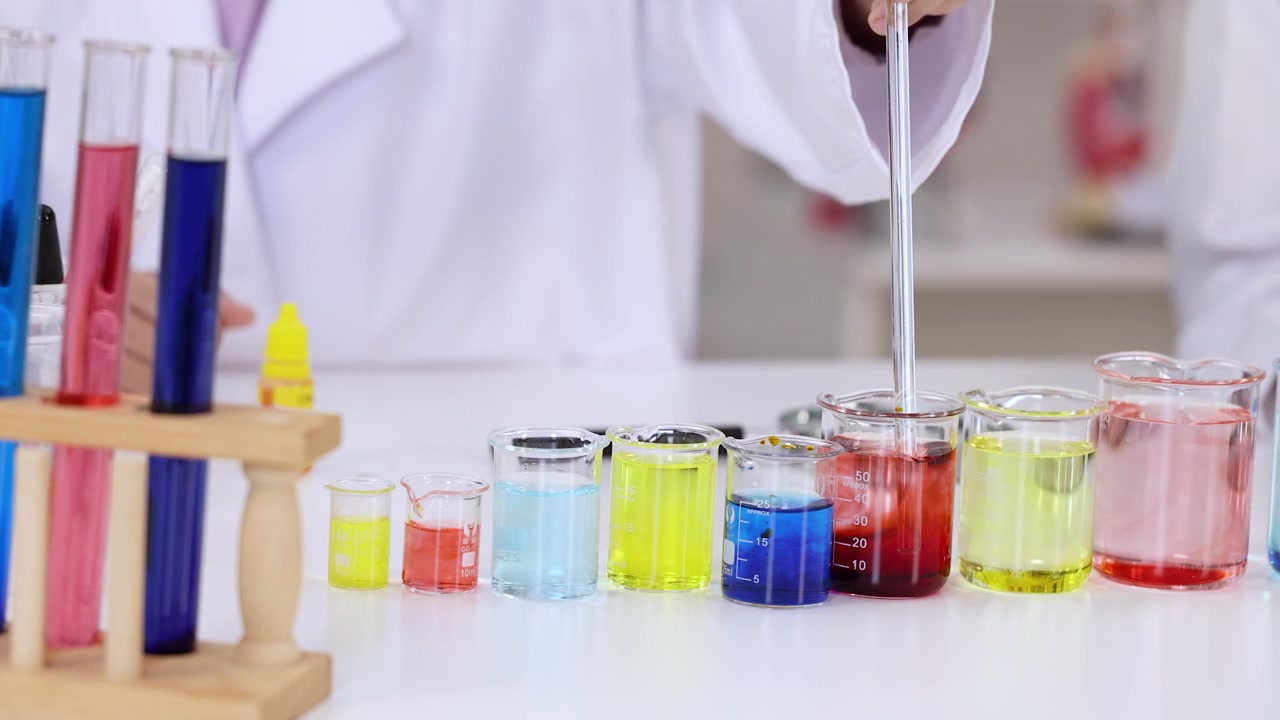 Uno scienziato in camice bianco usa una pipetta per mescolare soluzioni chimiche colorate.