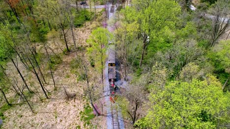 an aerial view of an 1860's steam passenger train traveling thru a wooded area on a lonely single rail road track