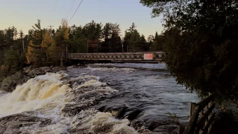 Toma-De-Carro-De-Los-Rápidos-Del-Río-Que-Fluyen-Hacia-La-Cascada,-El-Paisaje-Forestal-En-El-Fondo,-El-Estado-De-ánimo-De-La-Puesta-De-Sol