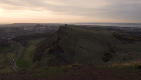 panning shot of edinburgh cityscape from the arturs seat mountain during sunset with wonderful colors and golden hour light with cars passing by down below