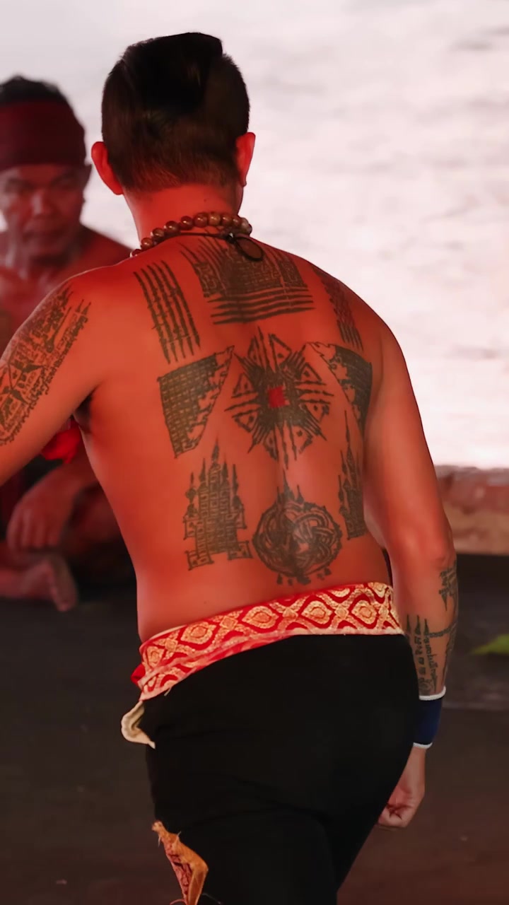 Combattente a torso nudo con tatuaggi intricati esegue movimenti tradizionali di arti marziali in una calda luce naturale.