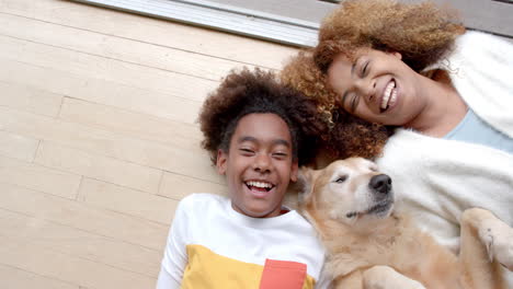 portrait of happy african american mother and son lying on floor, with their pet dog, slow motion