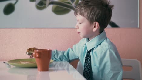 CU-Schoolboy-sits-at-the-table-in-school-uniform-and-has-breakfast-playing-before-going-to-school