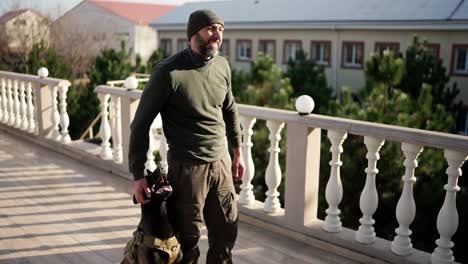 un hombre está de pie en la terraza con un perro de servicio en un collar de protección militar