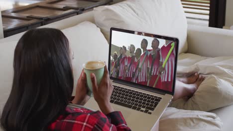 Composite-of-woman-sitting-at-home-holding-coffee-watching-hockey-match-on-laptop