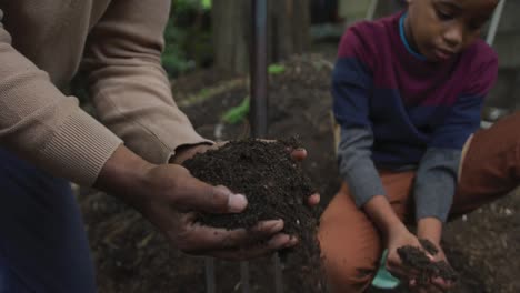 hombre afroamericano mayor feliz con su nieto plantando en el jardín