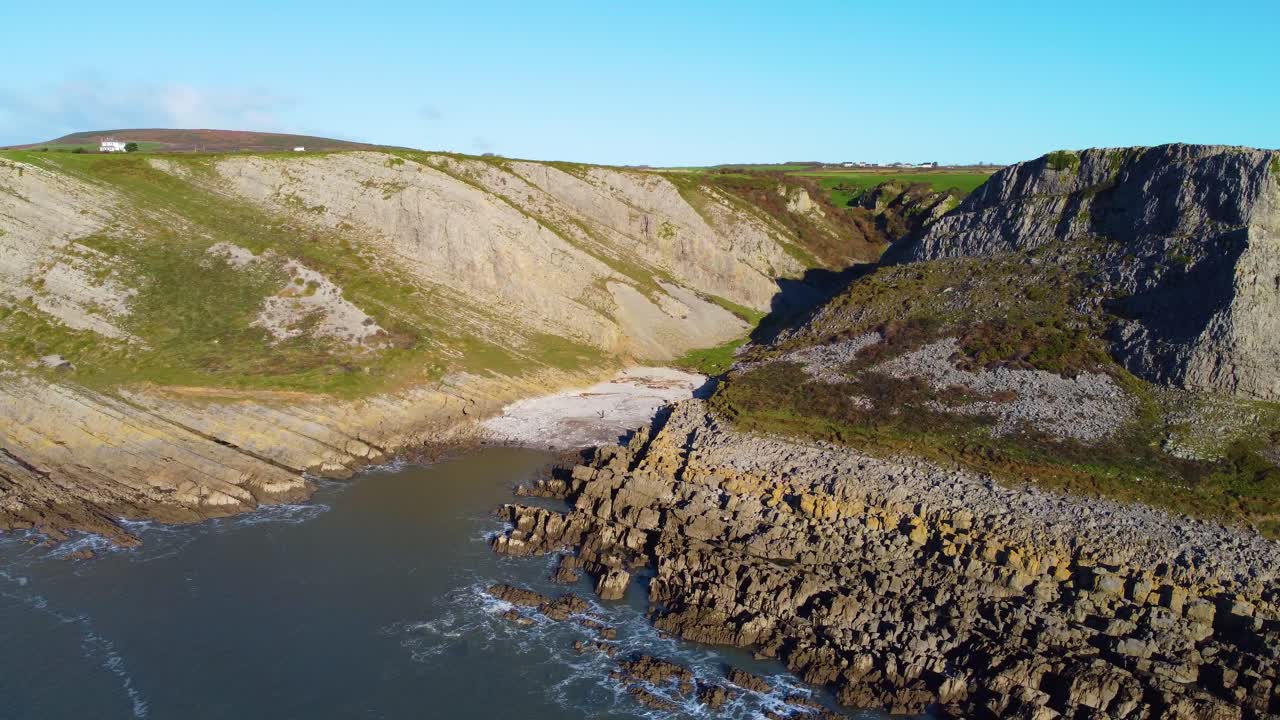 Aerial View Down Short Steep Valley as Drone Orbits Around Small Bay with Houses in Deep Background. Scenic Tourist Destination in Gower Peninsula, South Wales, UK