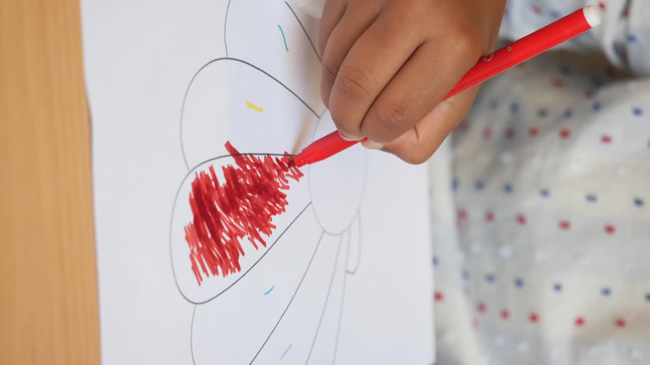 Child coloring a flower drawing with a red marker