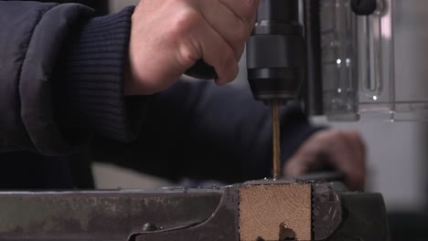 close-up-shot-of-man-operating-drilling-machine-drilling-multiple-holes-with-a-golden-drill-in-metal-plate-with-a-blurry-background