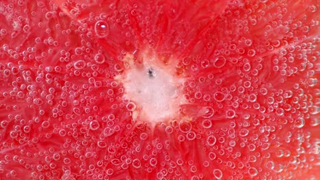 una rebanada de pomelo rojo maduro bajo el agua con burbujas de aire.