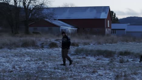 Indre-Fosen,-Trondelag-County,-Norway---On-the-Farm-in-November,-a-Man-Strolls-Slowly-with-His-Dog---Tracking-Shot