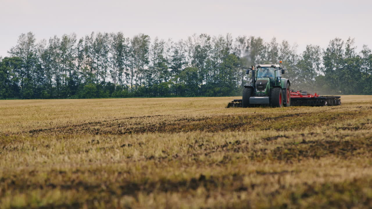 Un trattore ara il terreno nel campo, con uno stormo di uccelli che vola via.