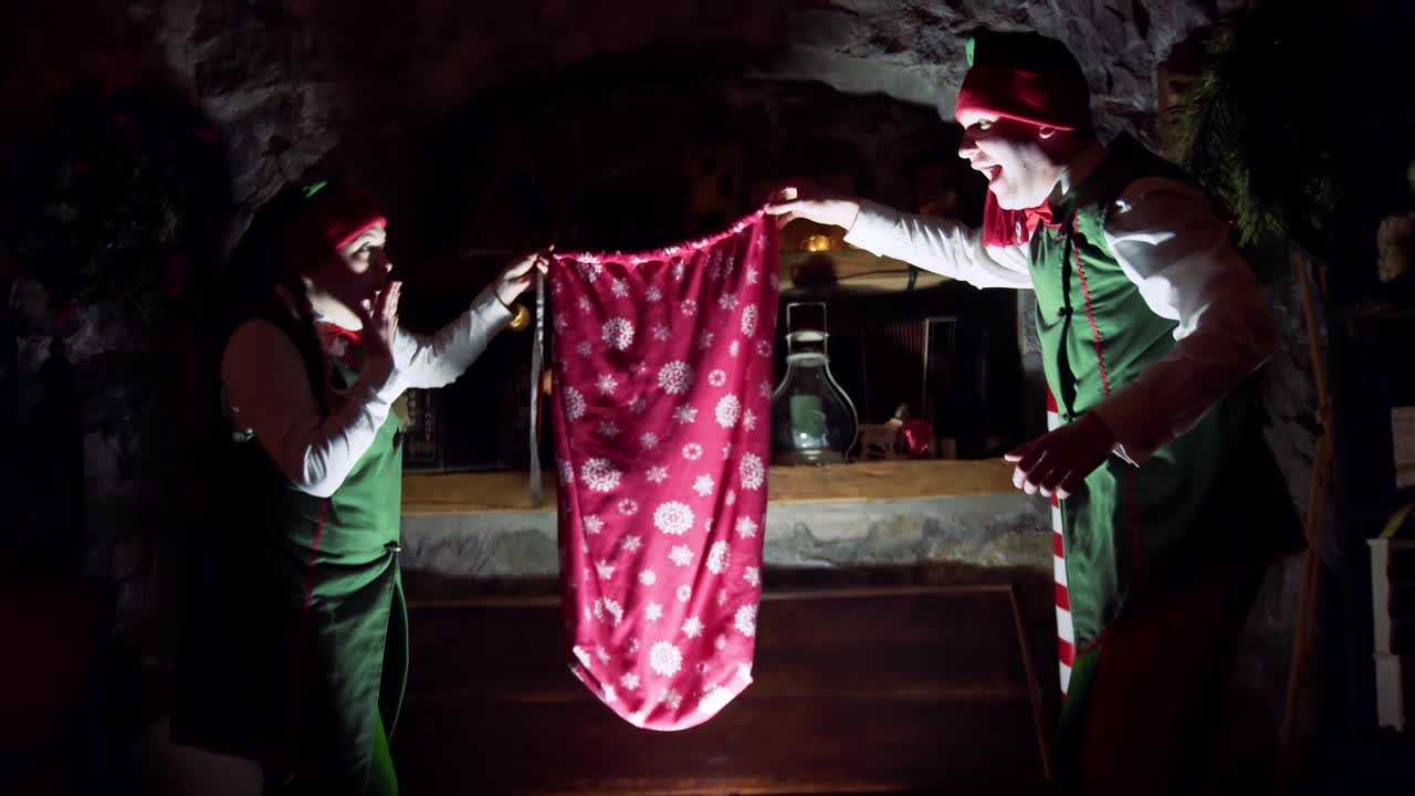 Elves in the dark room at Christmas. Santa's helpers are opening glowing old wooden box and taking out a red bag for presents at Christmas. Magic coffer