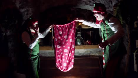 elves in the dark room at christmas. santa's helpers are opening glowing old wooden box and taking out a red bag for presents at christmas. magic coffer