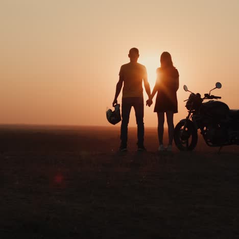 Silhouetten-Eines-Jungen-Paares-Bei-Sonnenuntergang,-Das-An-Ihrem-Motorrad-Steht