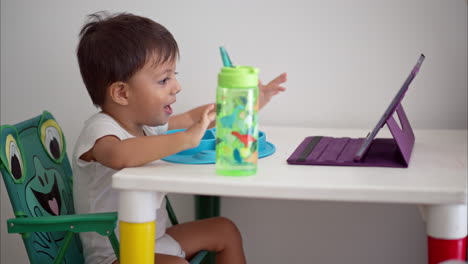 Lindo-Niño-Latino-Viendo-Una-Película-En-Una-Tableta-Mientras-Desayuna-Sentado-En-Una-Mesa-De-Bebé