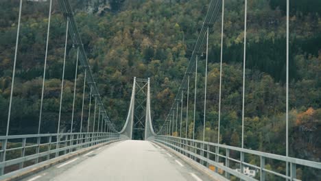 conduciendo por el estrecho puente colgante sobre el fiordo de hardanger y hacia las montañas cubiertas de bosques
