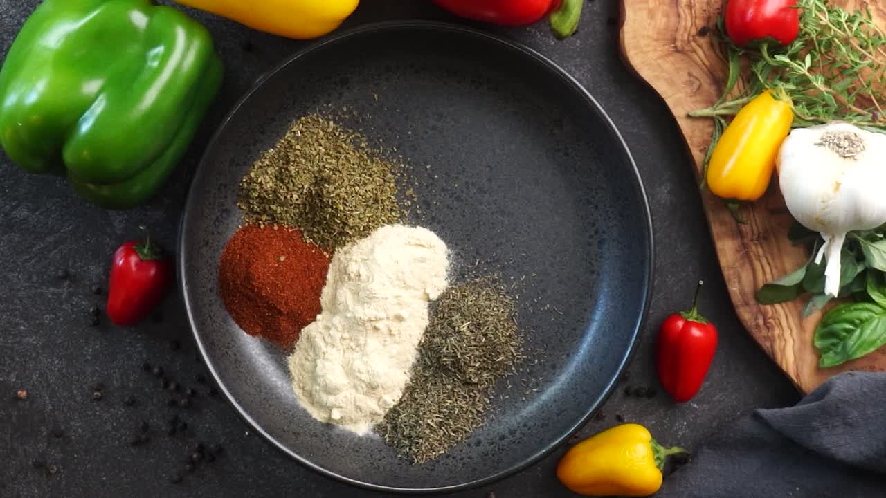 Making a vibrant Cajun Spice Blend, mixing red paprika, cayenne pepper, oregano, thyme, white garlic onion powder and black pepper in a bowl, creating a striking contrast against a black background.