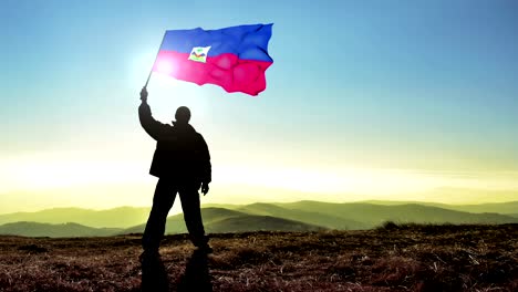 exitoso hombre silueta ganador agitando bandera de haiti en la parte superior del pico de la montaña. fondo de bucle cinemagraph