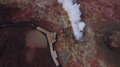 Person-observing-the-magnificent-steam-vent-rising-through-a-crater-in-red-lava-field,-Iceland