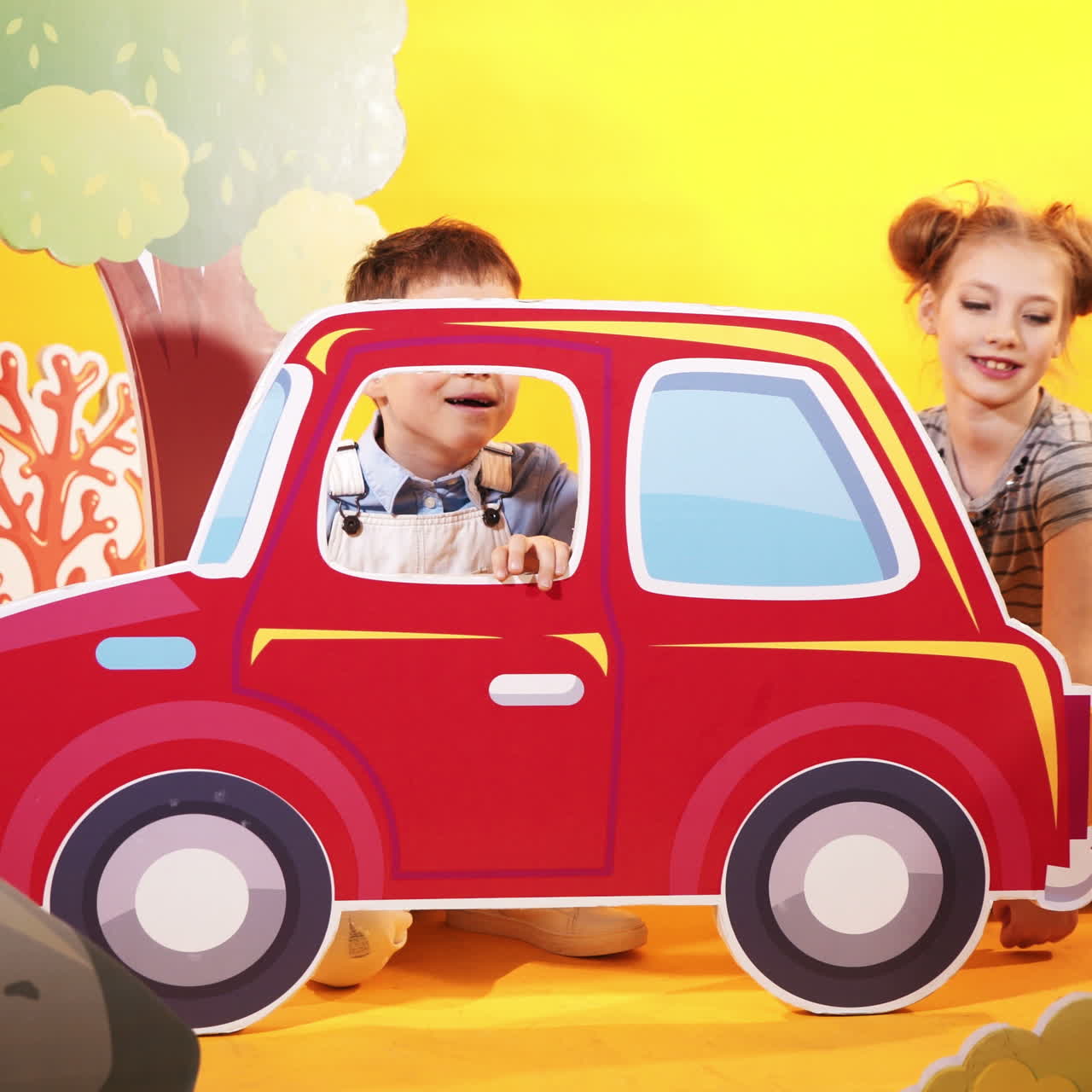 Funny children are playing with a big red car. Decorative background. Studio shooting of children