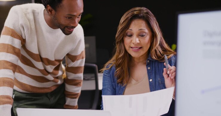 African American team reviewing findings, woman pointing pen, man coming from left studying laptop