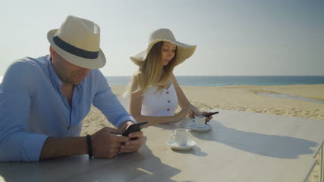 smiling couple using smartphones on beach