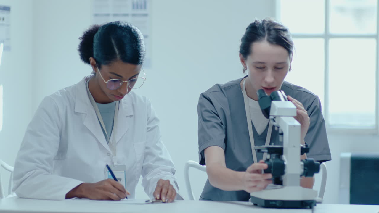 두 명의 여성 과학자들이 의학 실험실에서 현미경으로 연구를 하고 있습니다.