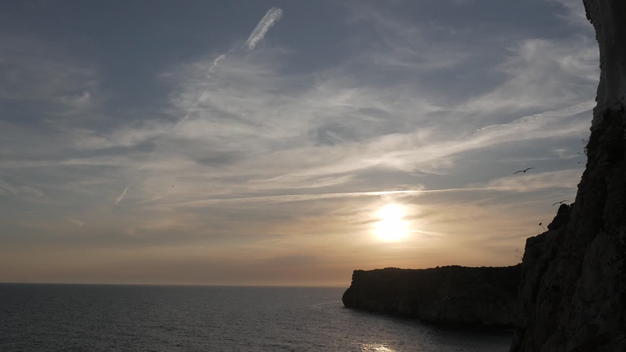 Golden sunset over the ocean at Cova D'En Xoroi, Menorca, with cliffs and birds in flight