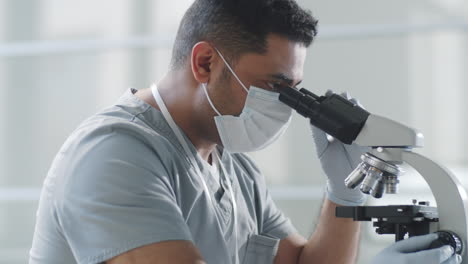 Hombre-Con-Máscara-Y-Guantes-Usando-Microscopio-En-Laboratorio