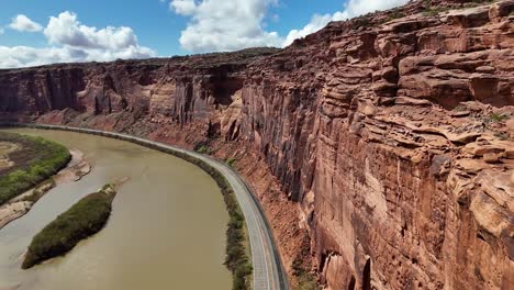 aerial view of highway next to river and tall cliffs, potash road in moab utah, colorado river, train tracks, blue sky with clouds, early spring, lower colorado scenic byway