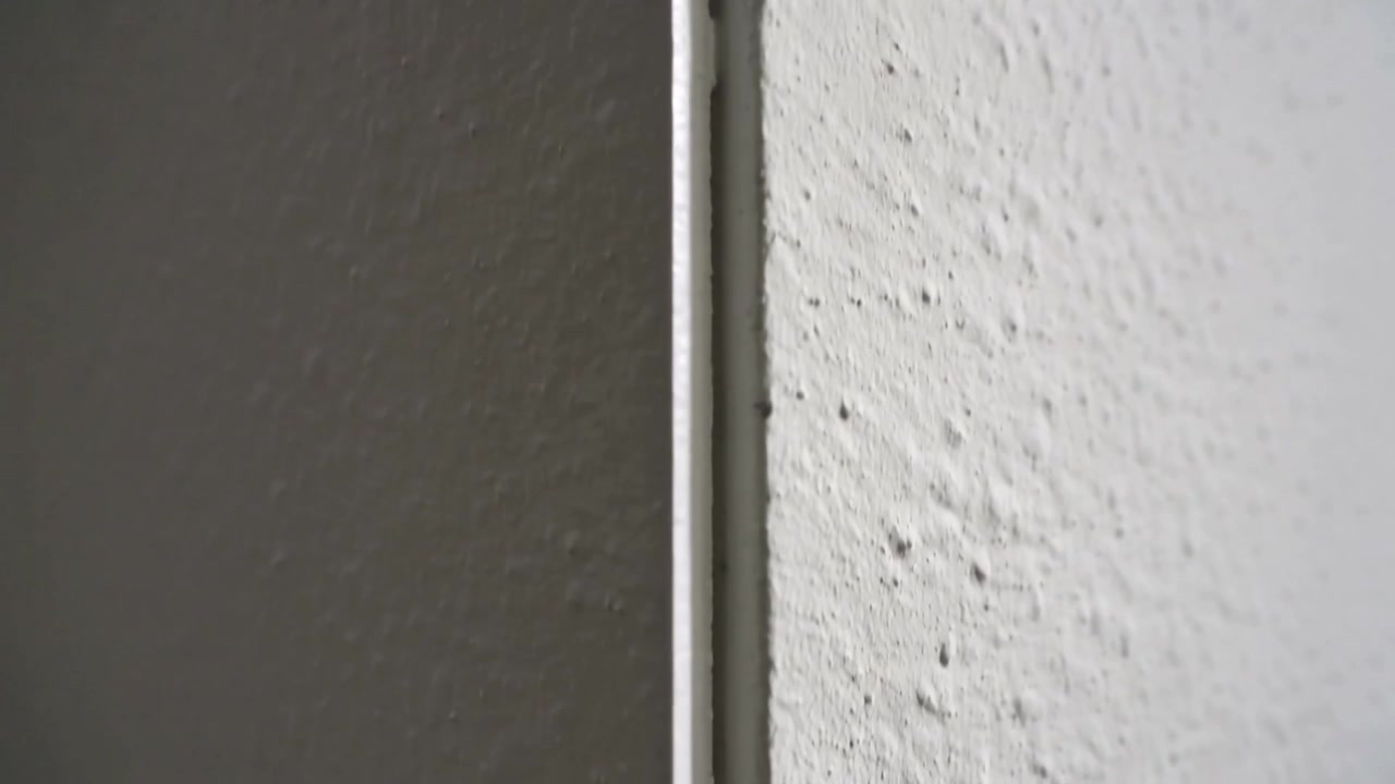 Cámara estabilizada revelando un ribete blanco centrado y una junta en la esquina de la habitación, exponiendo una pared texturizada.