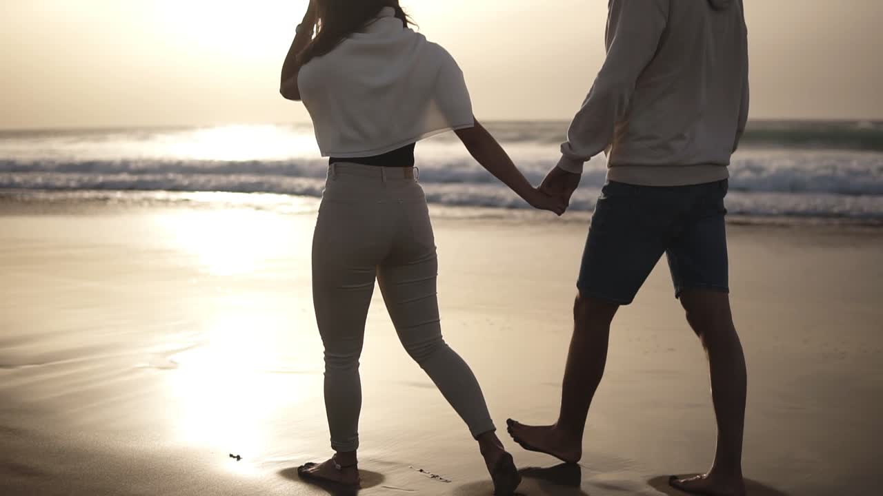 해변에서 맨발로 걸어가는 편안한 커플. 그들은 빈, 평화로운 해안에서 함께 시간을 보내고 있습니다. 젊은 남녀가 열대 해변에서 신혼여행을 보내고 있습니다. 희귀한 전망