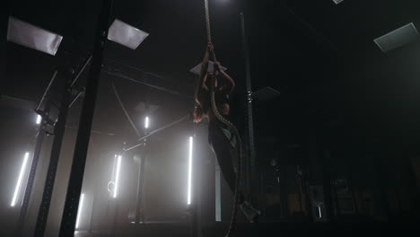 workout in gym woman is climbing on rope in fitness center power training for keeping fit