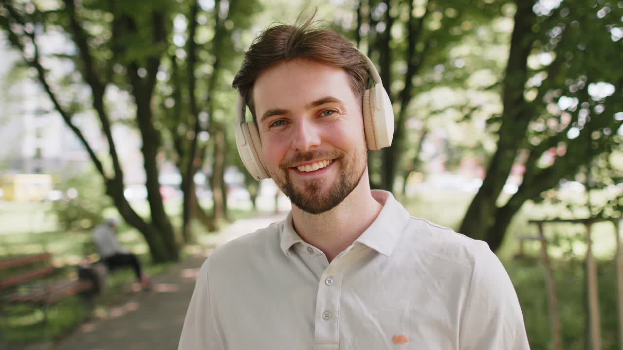 Glad løper jogger smilende mann tar på trådløse hodetelefoner øretelefoner nyter musikk i parken utendørs