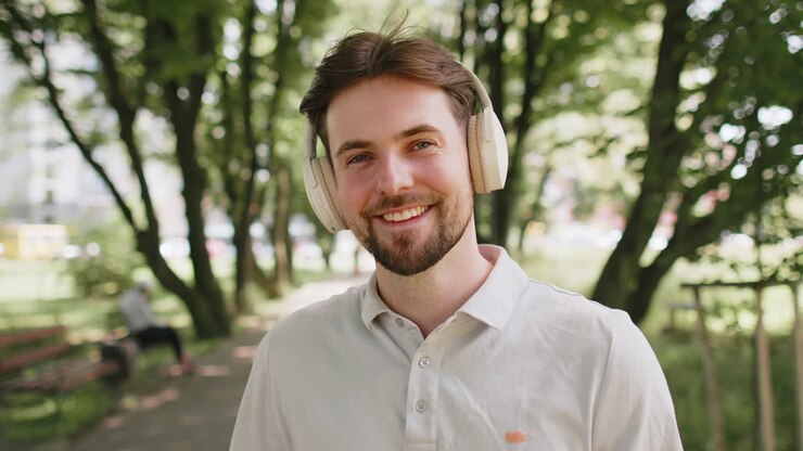 Glad løper jogger smilende mann tar på trådløse hodetelefoner øretelefoner nyter musikk i parken utendørs
